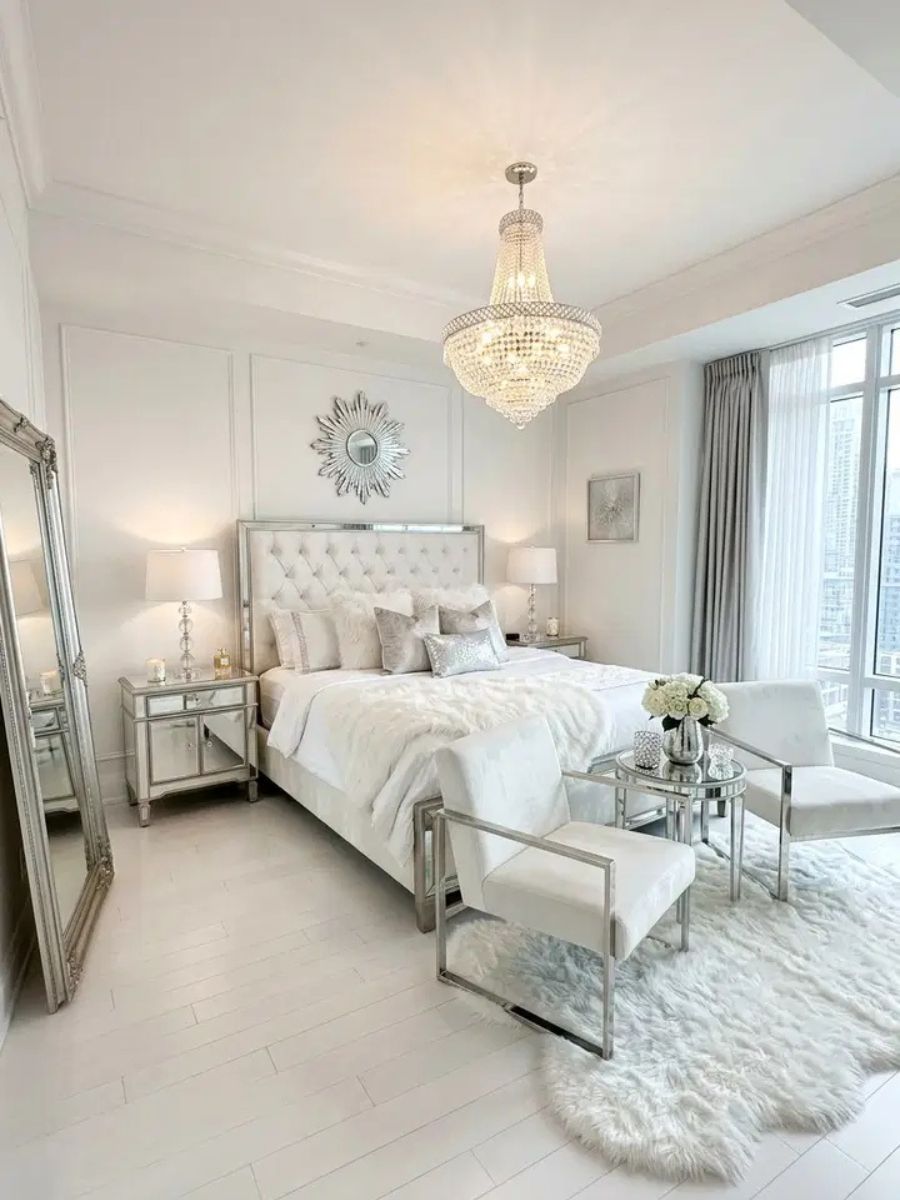 White glam bedroom with crystal chandelier, mirrored nightstands and faux fur rug
